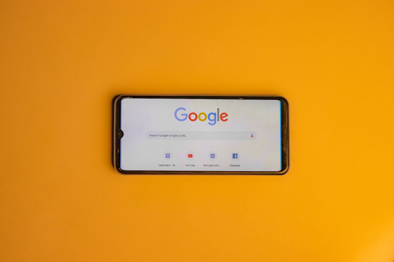 Services Smartphone displaying Google search page on a vibrant yellow background.