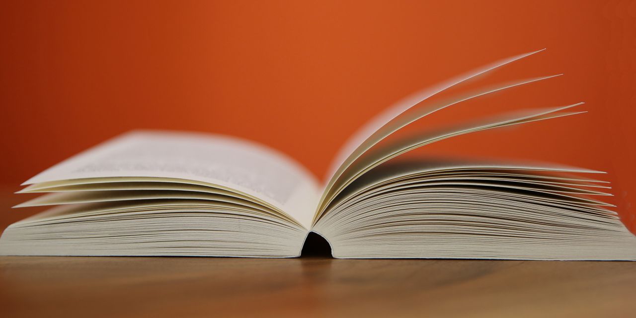About An open book with pages turning against a vibrant orange background, symbolizing knowledge and education.